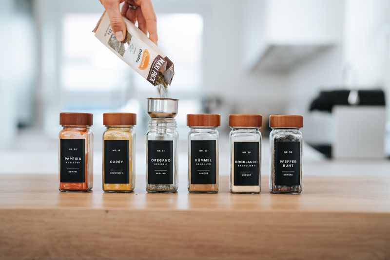 Eine Person schüttet einen Beutel Gewürze in ein Gewürzglas.