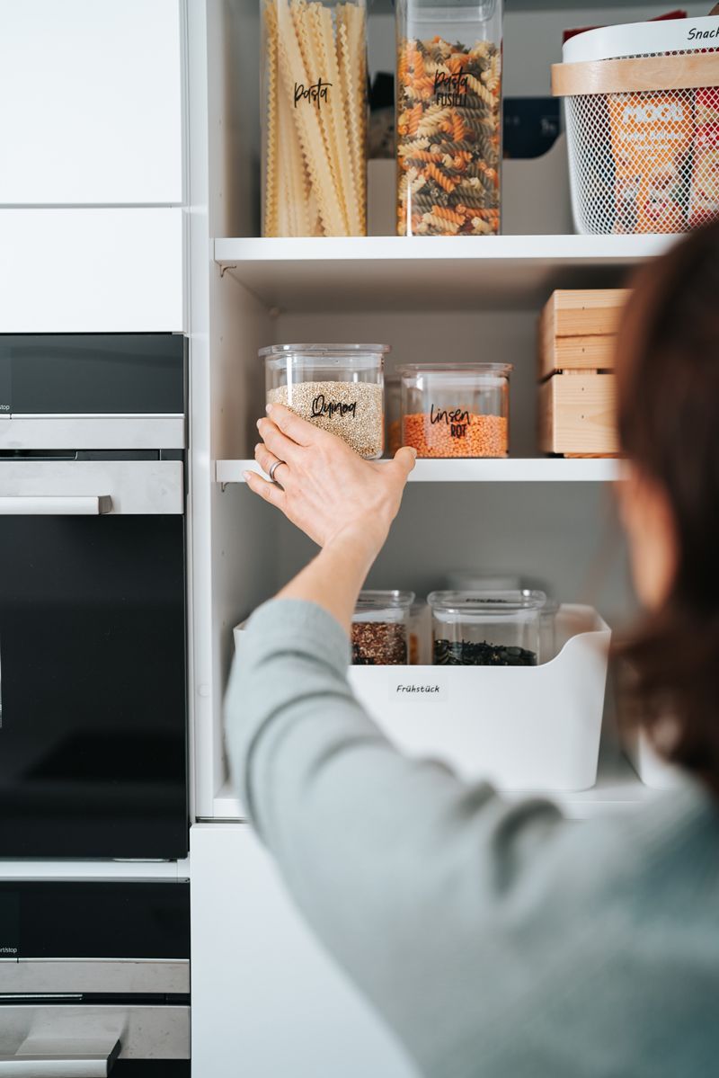 Eine Frau greift in einer Speisekammer nach einem Behälter.