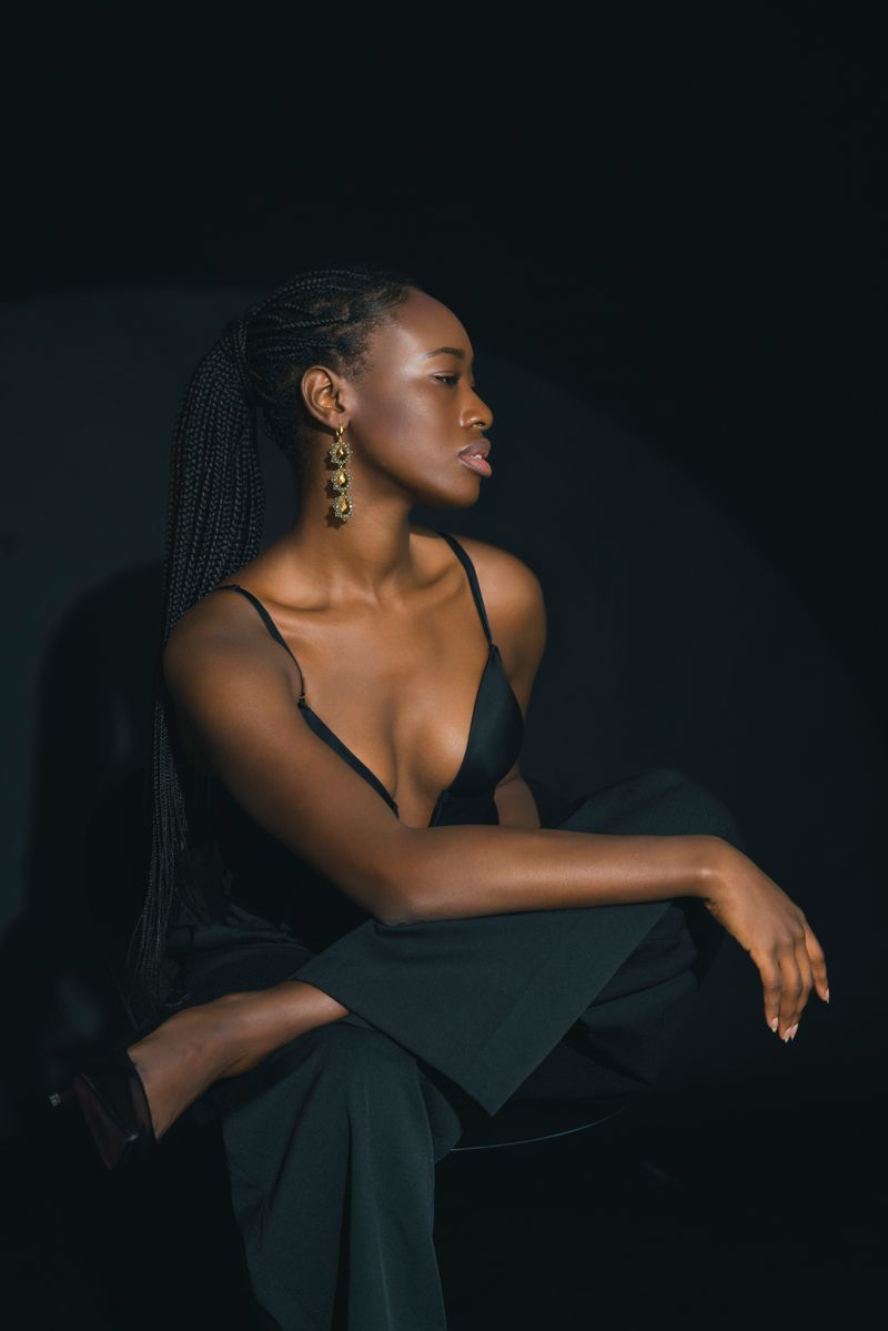 Eine Frau in einem schwarzen Kleid sitzt mit übereinandergeschlagenen Beinen auf einem Stuhl.