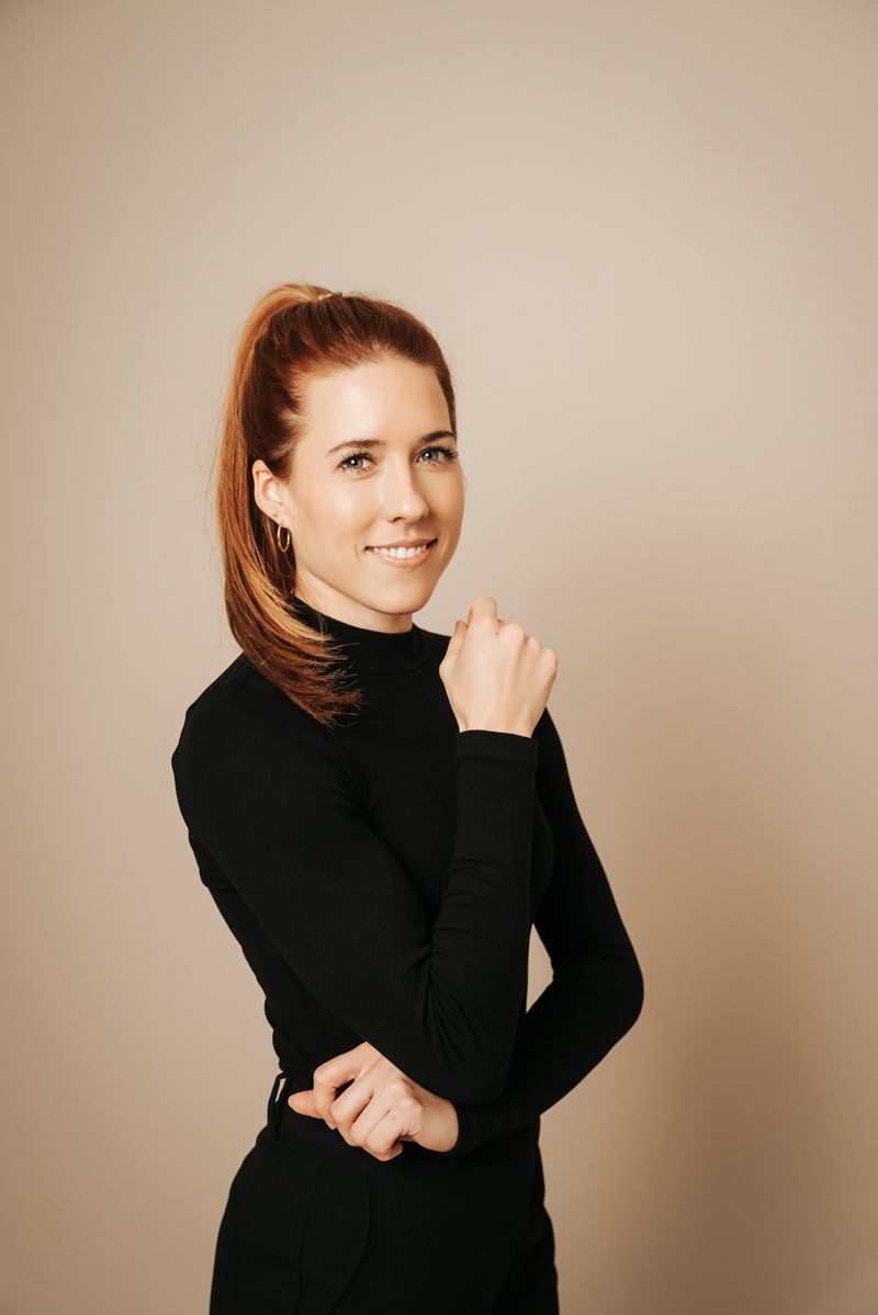 Eine Frau in einem schwarzen Kleid posiert für ein Foto und legt die Hand auf ihr Kinn.