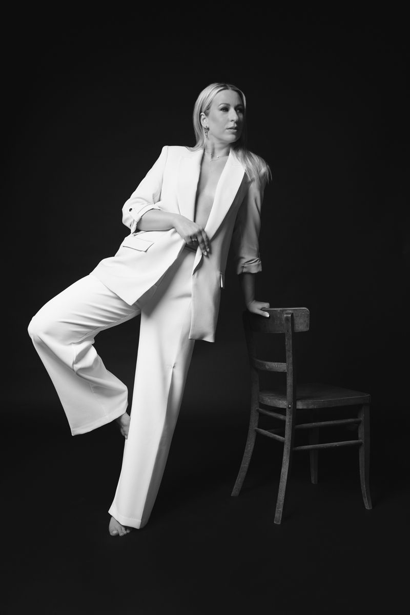 Eine Frau in einem weißen Anzug lehnt auf einem Stuhl.