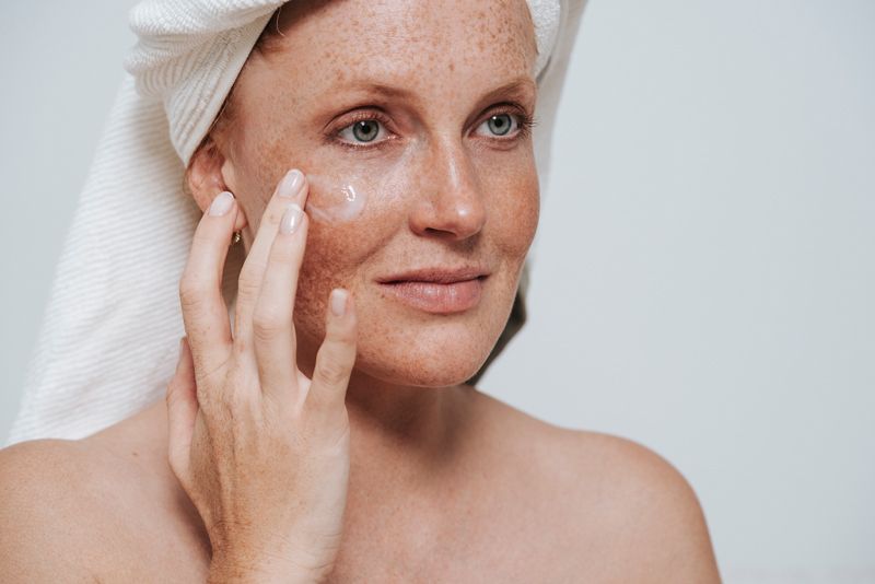 Eine Frau hat ein Handtuch um den Kopf gewickelt und cremt ihr Gesicht ein.