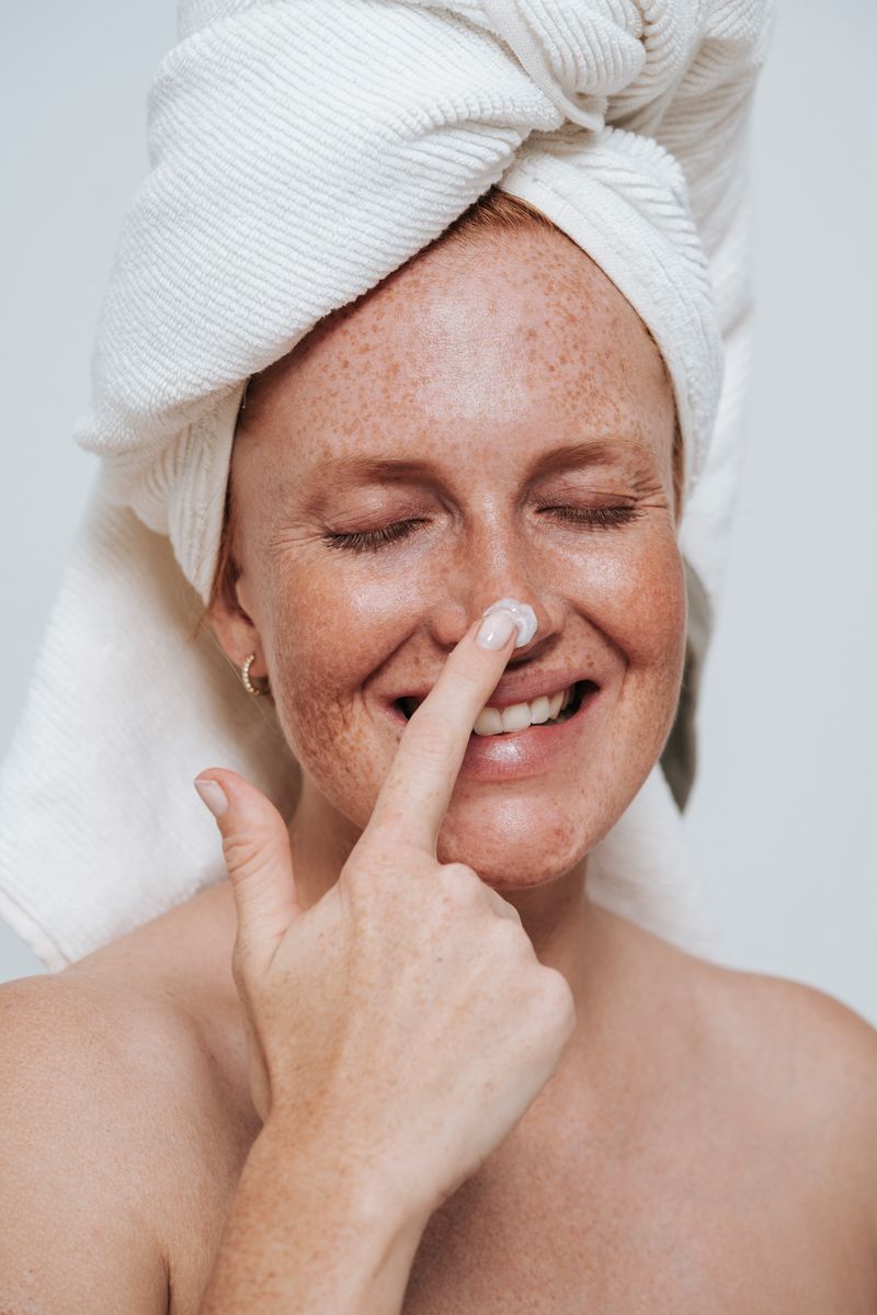 Eine Frau hat ein Handtuch um den Kopf gewickelt und cremt ihre Nase ein.
