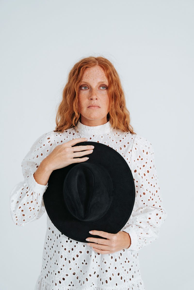 Eine Frau in einem weißen Kleid hält einen schwarzen Hut.