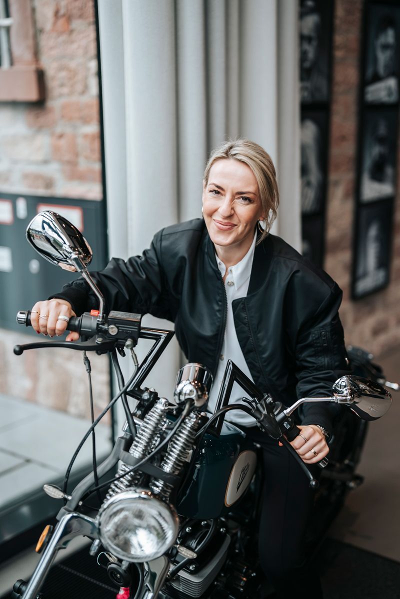 Eine Frau in einer schwarzen Jacke sitzt auf einem Motorrad.