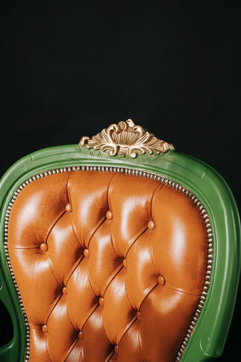 Ein grüner Stuhl mit Sitzfläche und Rückenlehne aus braunem Leder auf schwarzem Hintergrund.