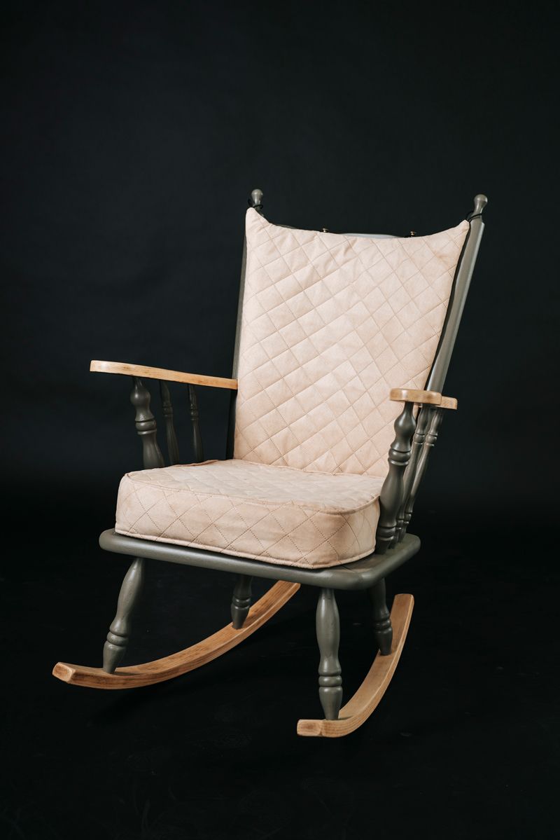 Auf einem schwarzen Hintergrund steht ein Schaukelstuhl mit einem Kissen darauf.