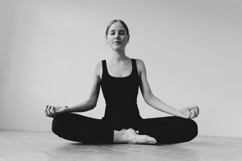 Eine Frau sitzt mit geschlossenen Augen im Lotussitz auf dem Boden.