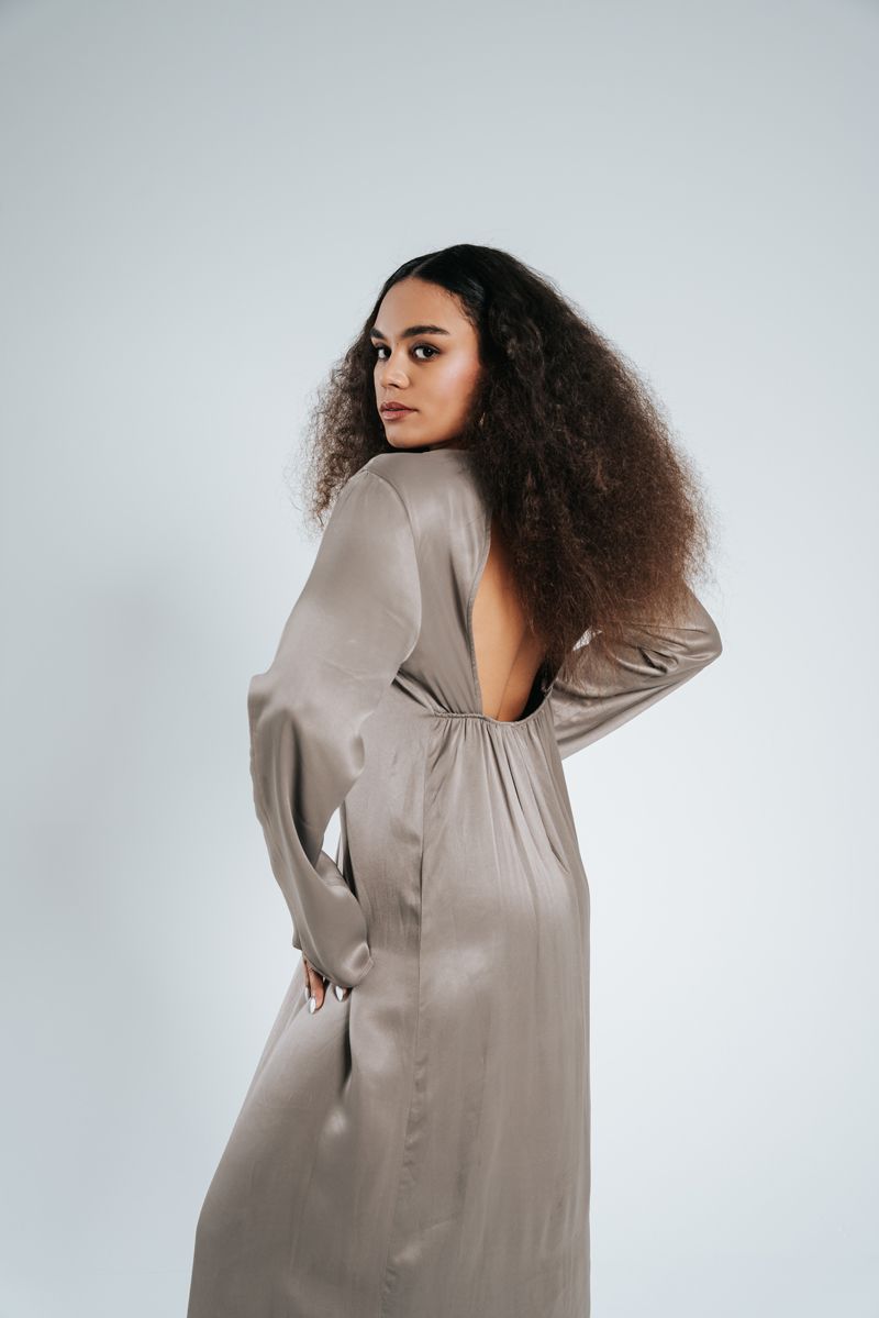 Eine Frau steht in einem langen Satinkleid mit offenem Rücken.