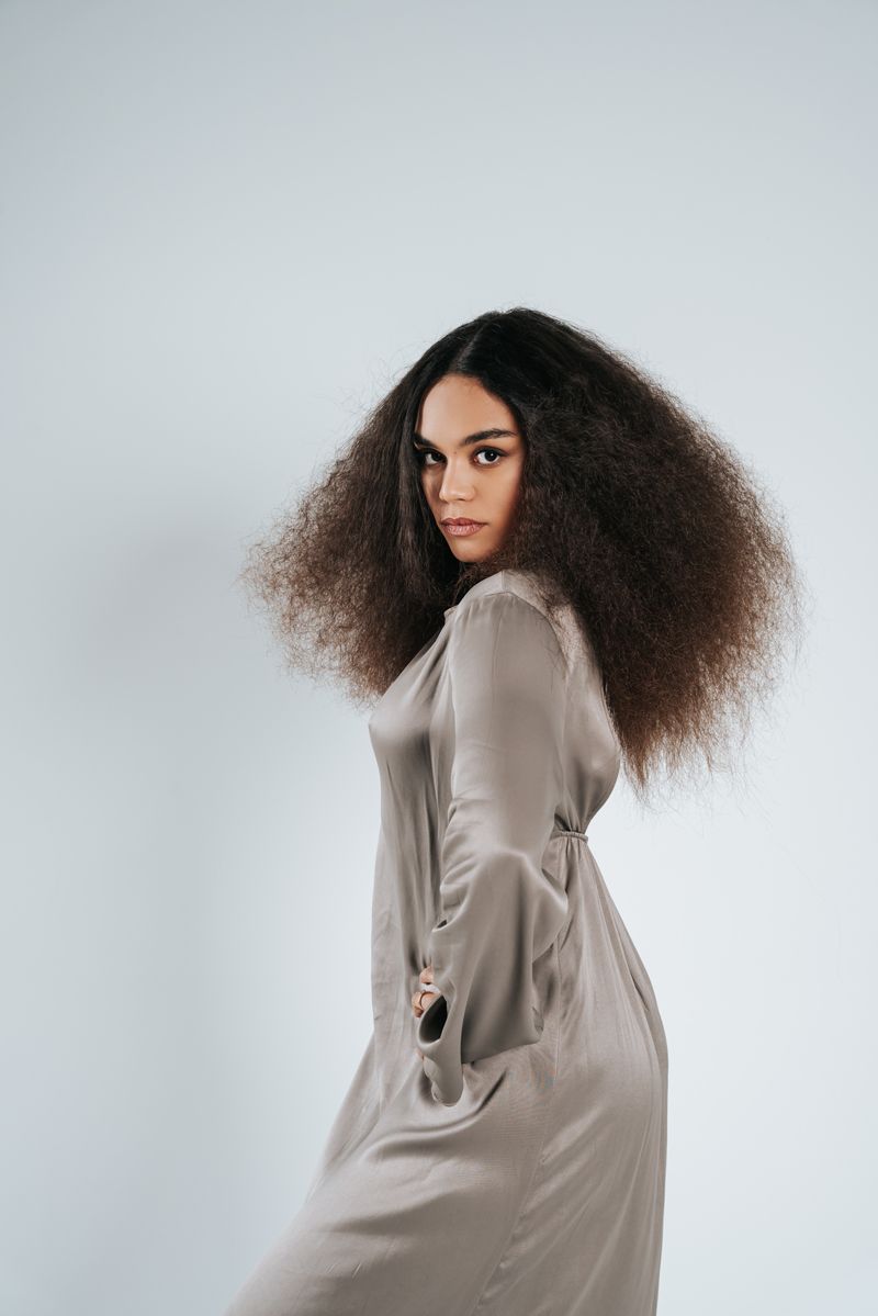 Eine Frau mit lockigem Haar trägt ein langes Satinkleid.