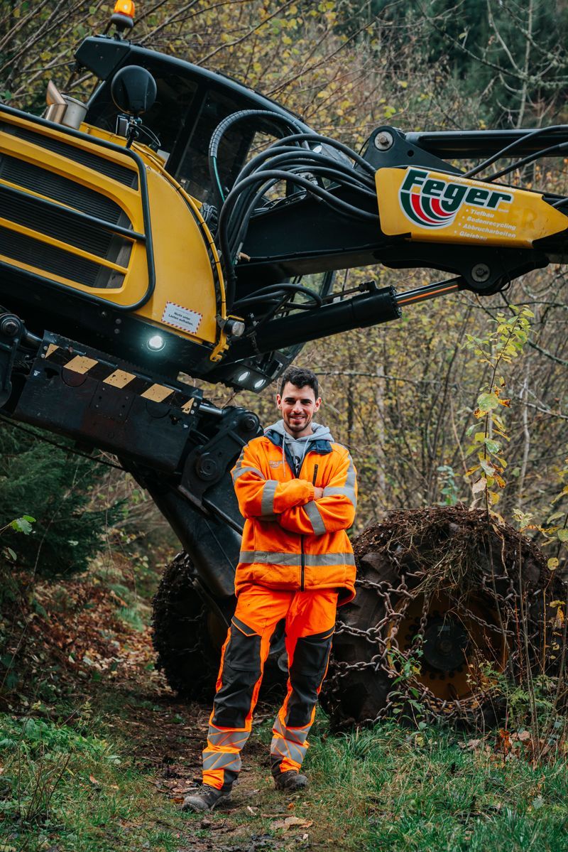 Ein Mann in orangefarbenen Hosen steht vor einer großen Maschine.