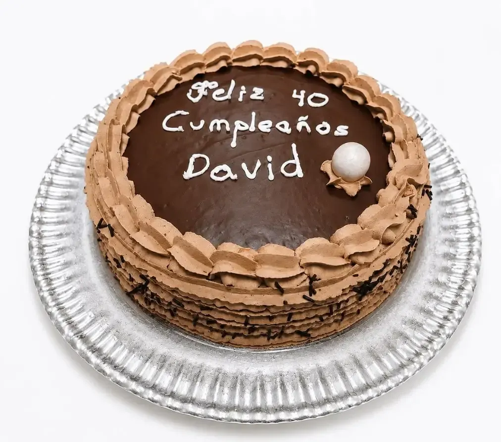 Tarta de chocolate de cumpleaños en una bandeja plateada, decorada con letras blancas que dicen “Feliz 40 cumpleaños David”.