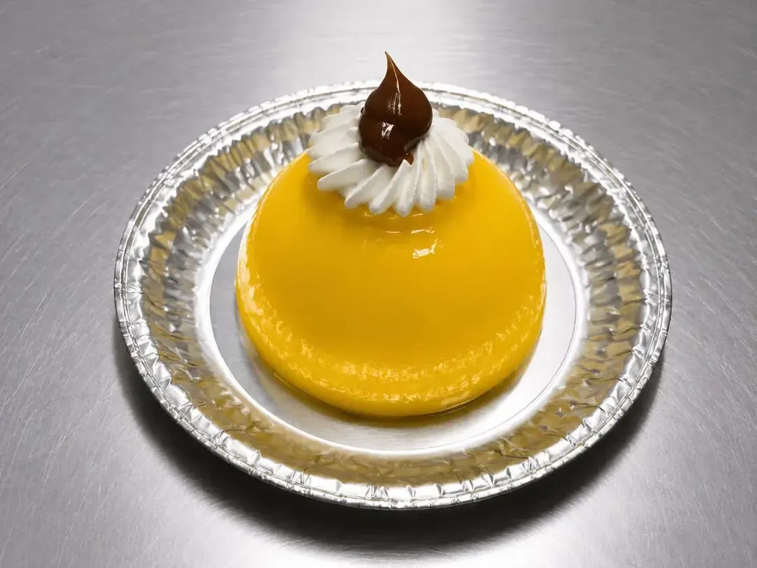 Postre amarillo con crema batida y decoración de chocolate en un plato de plata.
