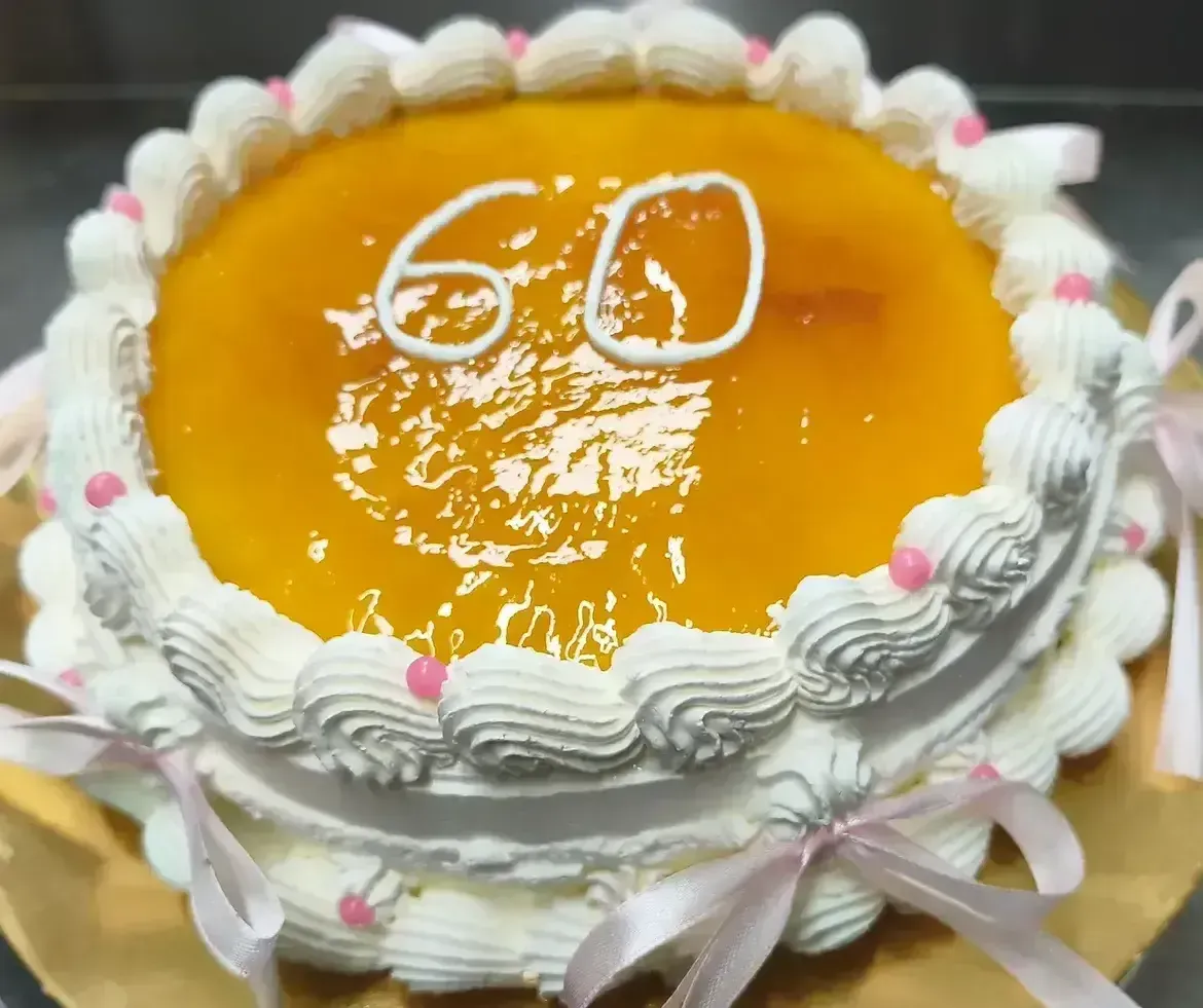 Tarta de celebración glaseada con naranja, con glaseado blanco batido y el número 60 encima.