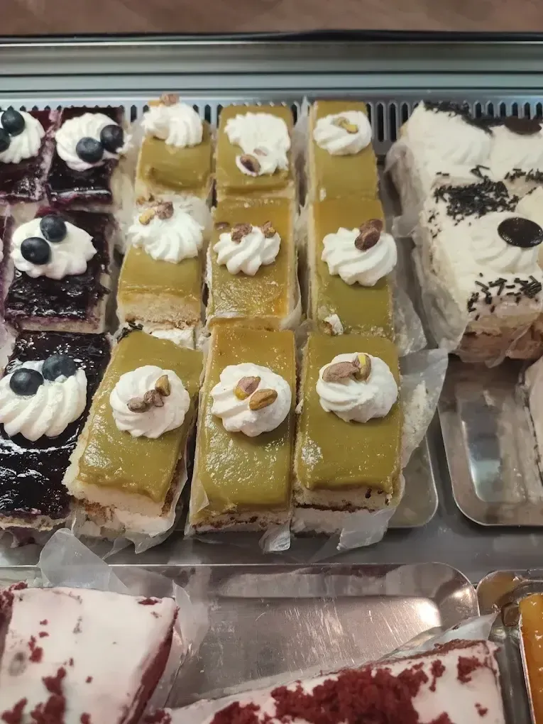 Bandeja de barritas de postre variadas cubiertas con nata montada y frutos rojos en un expositor de pastelería.