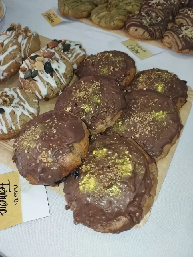 Variedad de pasteles decorados sobre una mesa, incluyendo dulces redondos cubiertos de chocolate con frutos secos y glaseado.