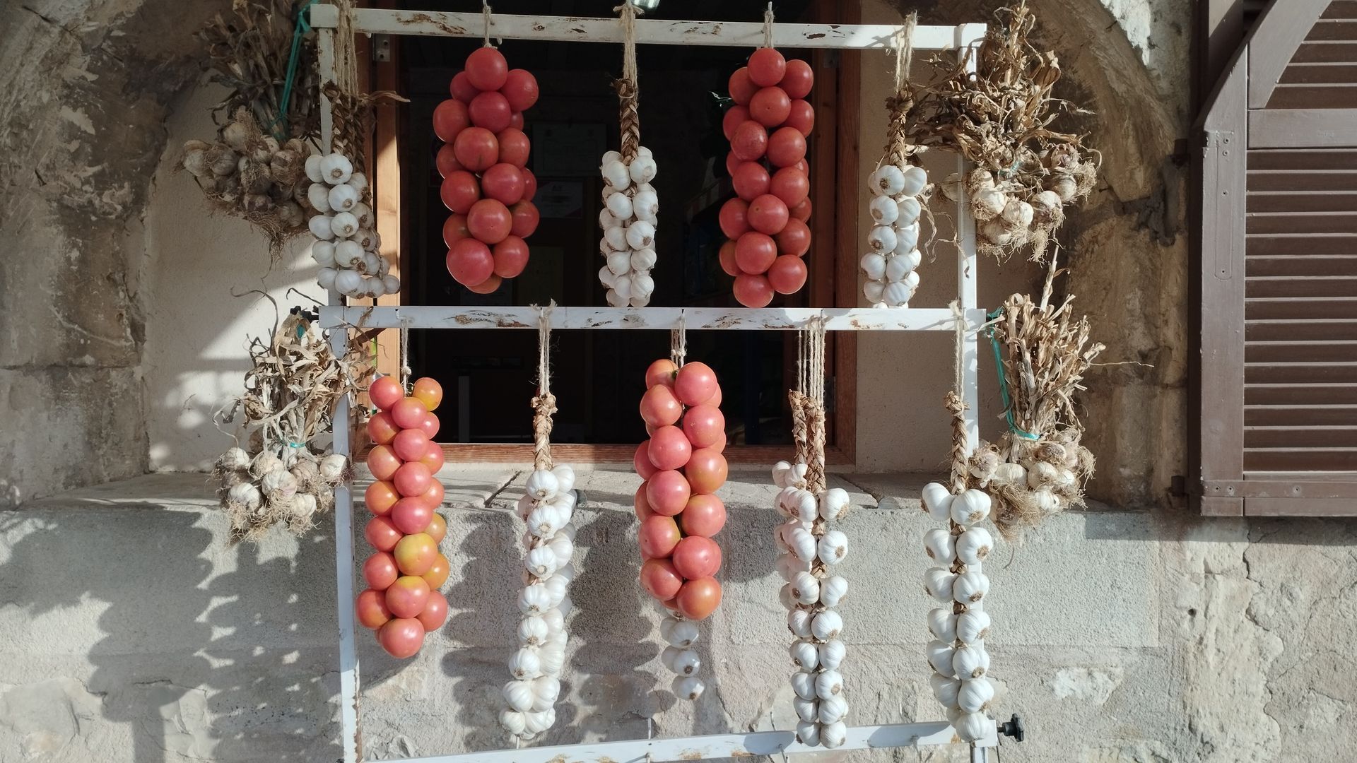 Una mujer compra en un puesto de mercado con ajo, calabazas y otros productos. Hay otros compradores presentes.
