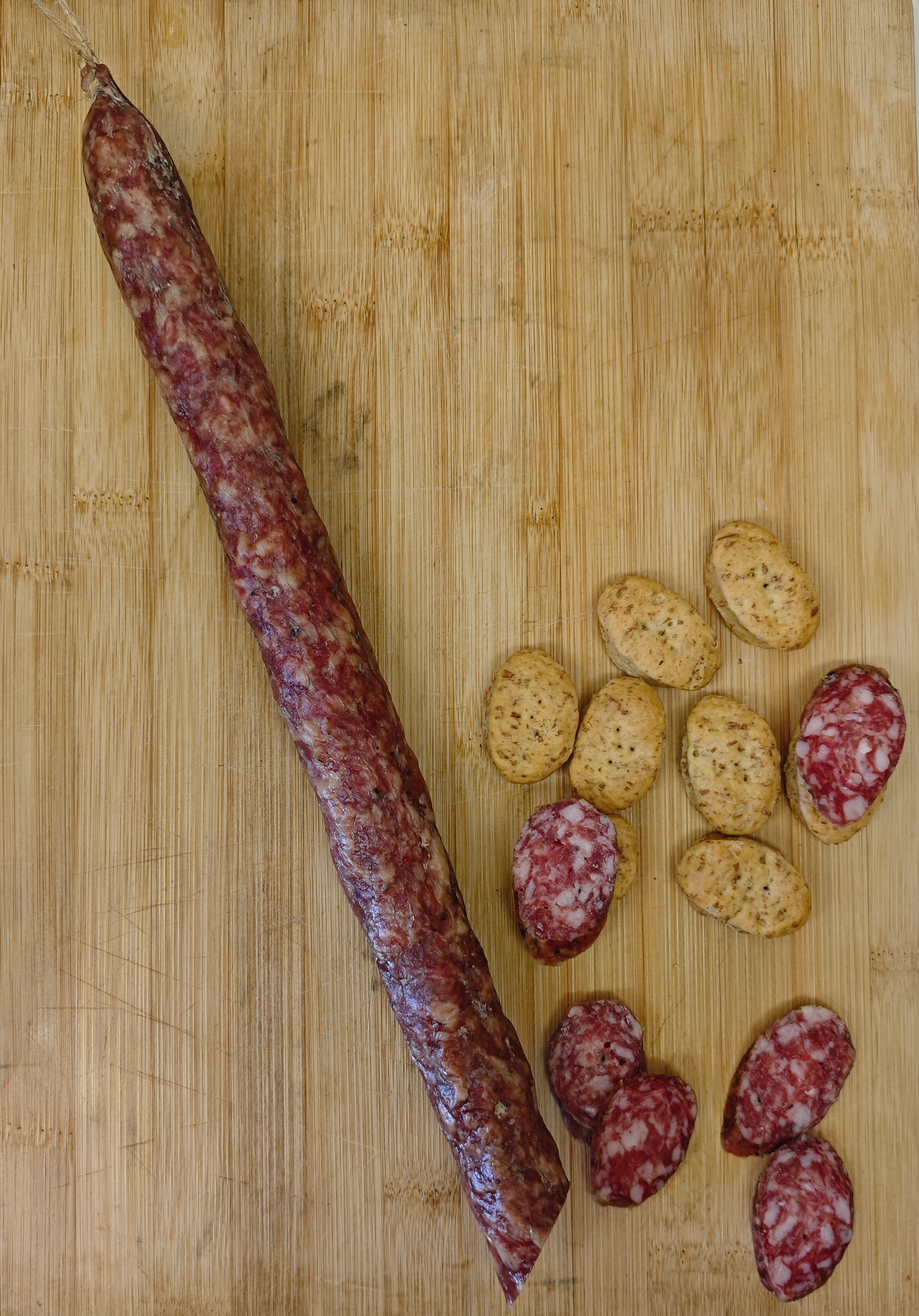 Palitos de salami largos y trozos cortados con pequeñas galletas sobre una tabla de cortar de madera.