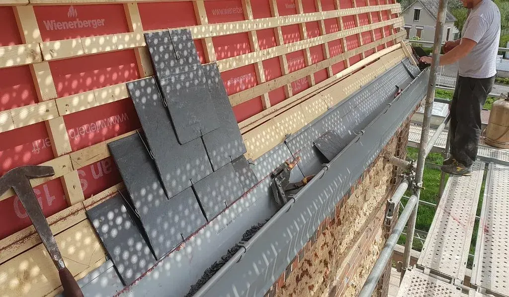 Un artisan sur de l'échafaudage pose de l'ardoise sur un toit.