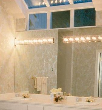 Un mueble de baño con un espejo grande, dos lavabos y apliques de luz horizontales brillantes montados sobre el espejo.