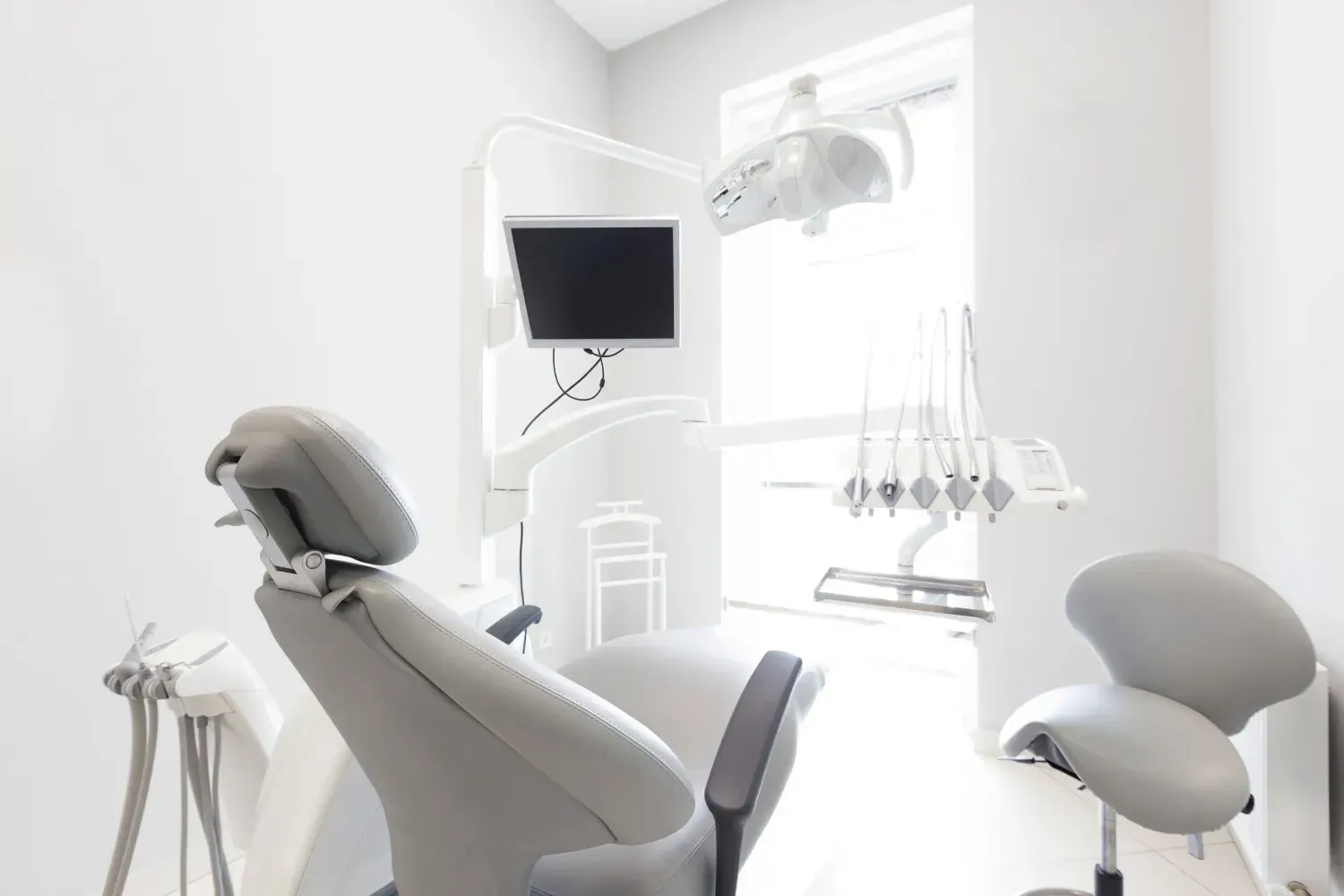 Un consultorio dental luminoso y moderno con un sillón gris para el paciente, un taburete para el dentista.