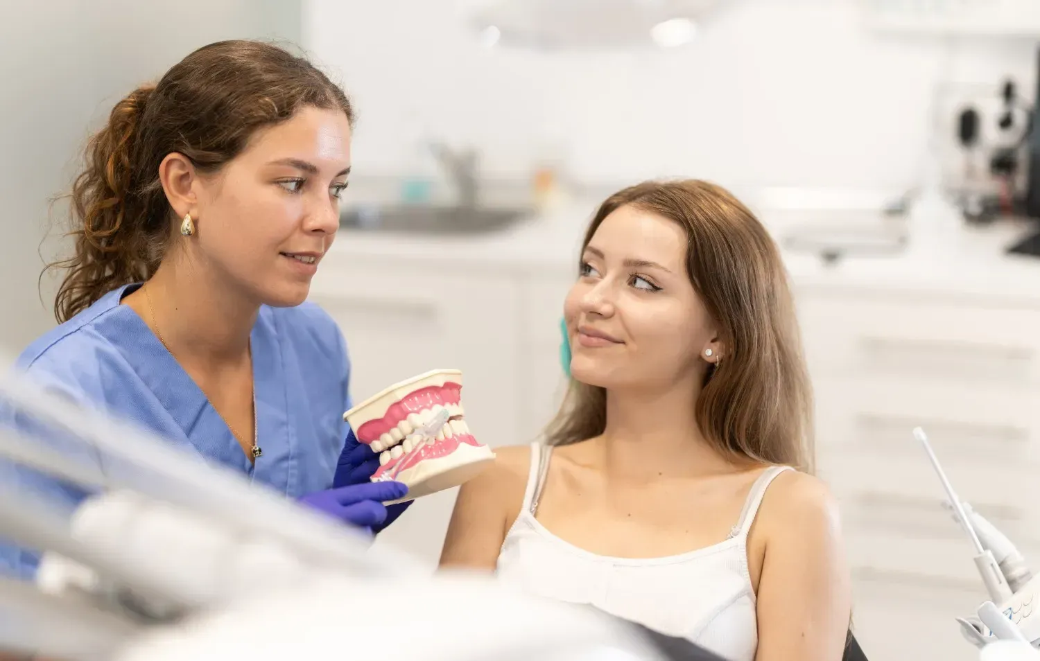 Un profesional con bata azul, sosteniendo un modelo dental, explica los cuidados dentales a un paciente.