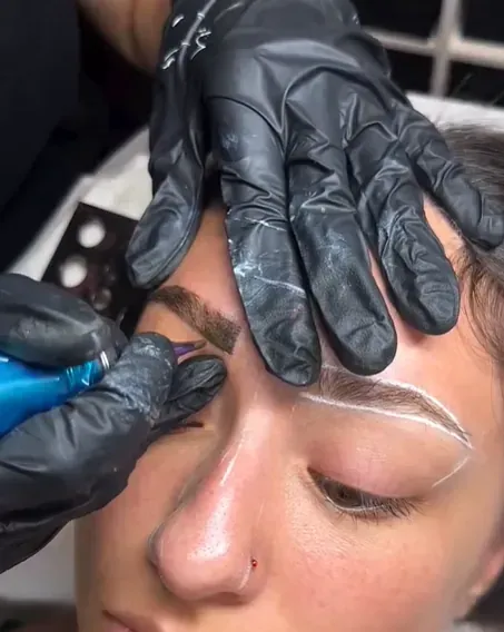 Una mujer se está tatuando las cejas con una máquina.