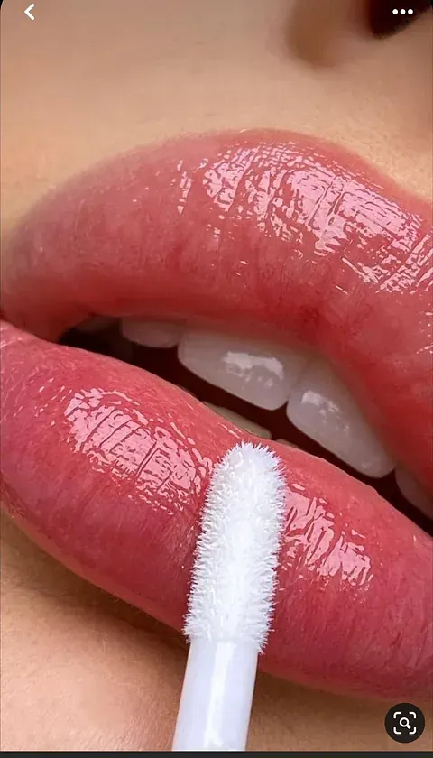 Una mujer se aplica brillo de labios en los labios con un pincel.