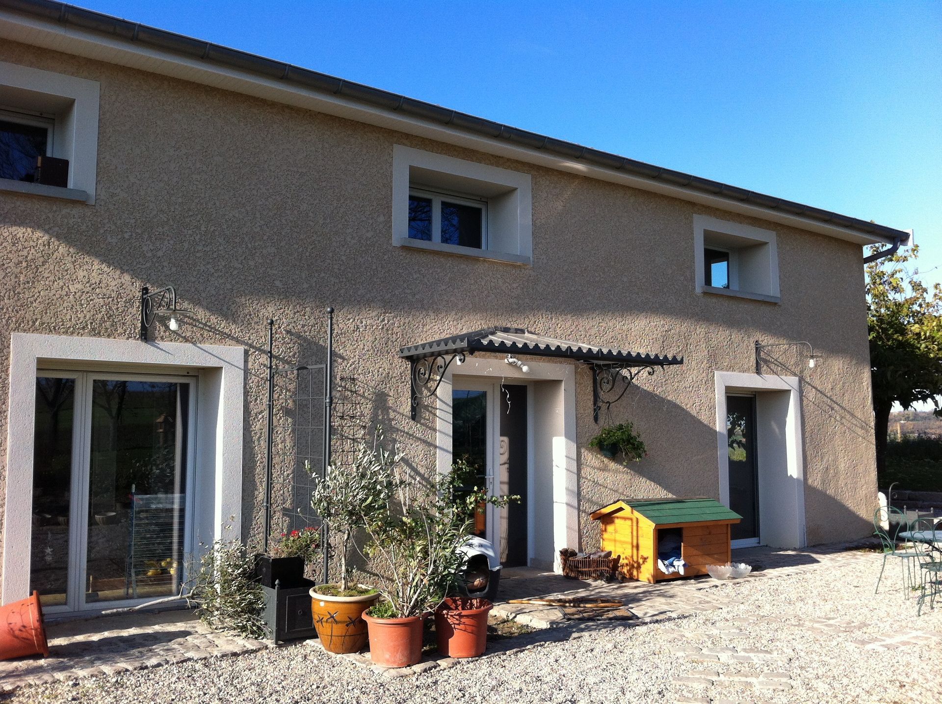 Maison à deux étages avec façade en stuc, fenêtres à cadre blanc et petit auvent métallique.