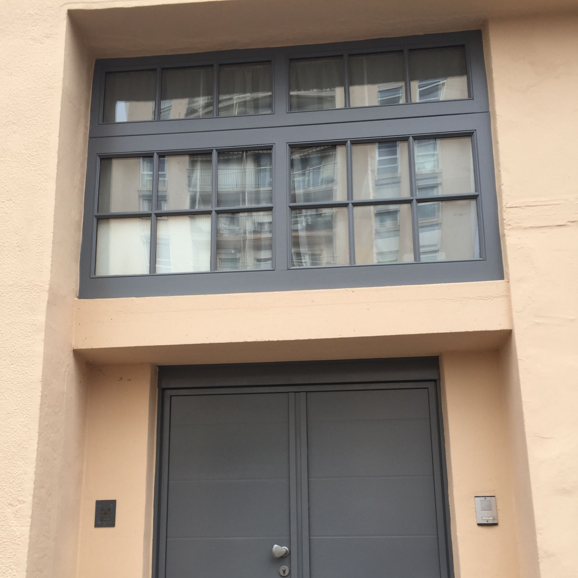 Porte grise et fenêtre à plusieurs carreaux encastrées dans une façade d'immeuble.
