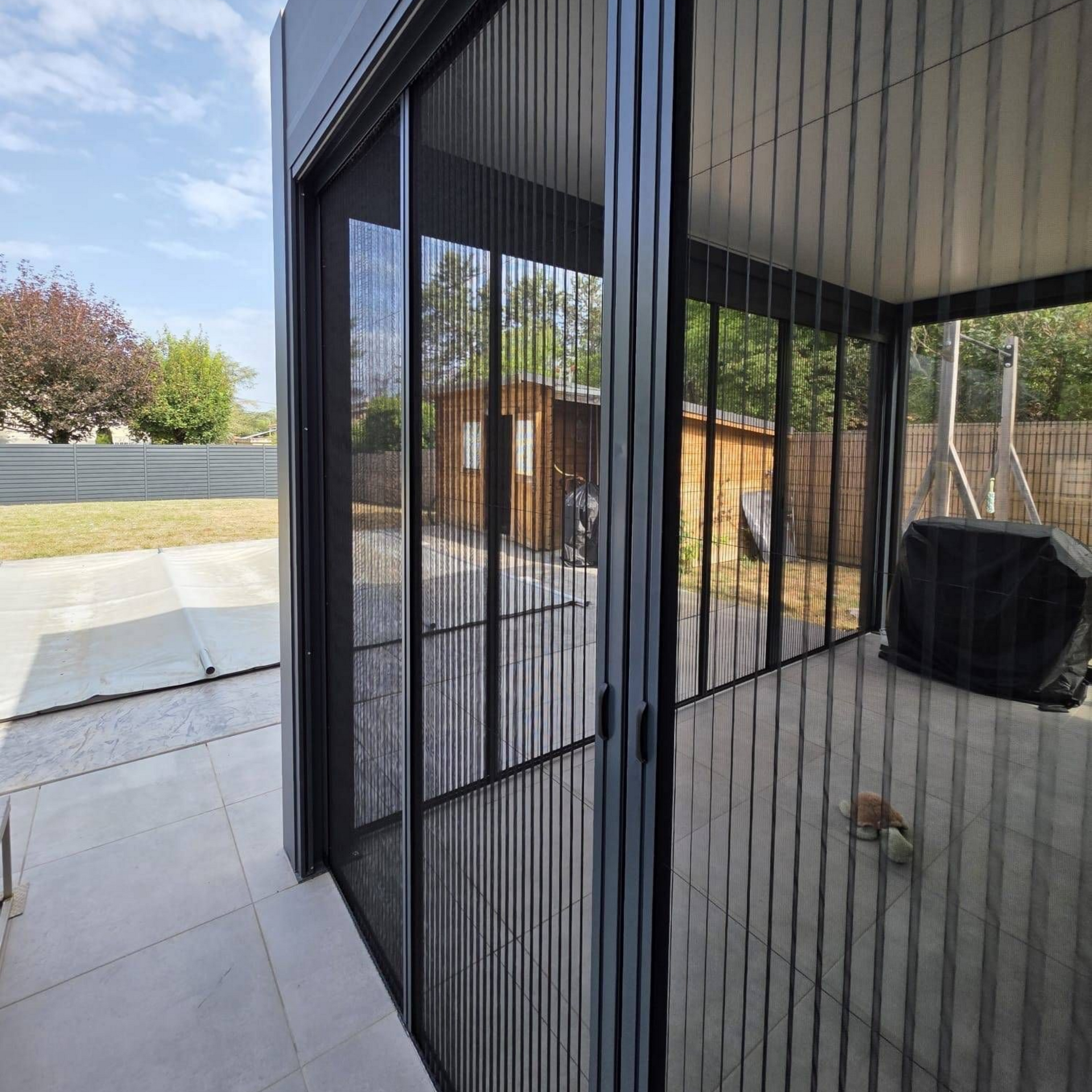 Porte moustiquaire noire sur une terrasse donnant sur un jardin.