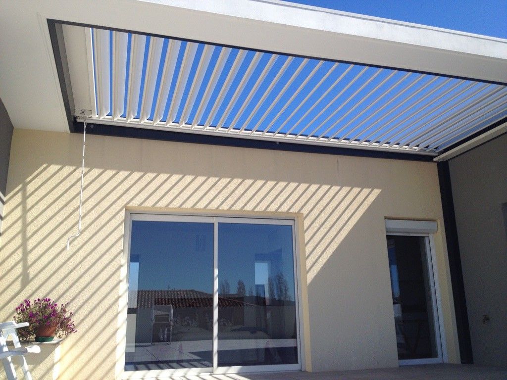 Vue extérieure d'une maison avec une pergola offrant de l'ombre à une terrasse.
