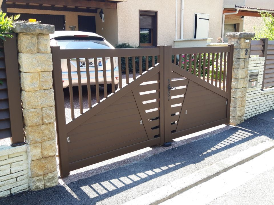 Portail d'allée en métal marron à motif diagonal, flanqué de piliers en pierre.