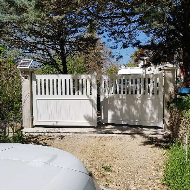Portail blanc ouvert donnant sur une allée. Panneau solaire sur le poteau de gauche.