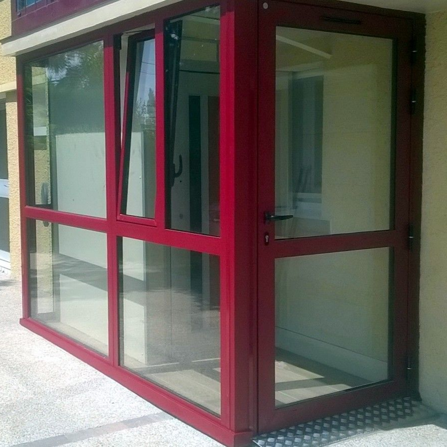 Une véranda vitrée à cadre rouge avec une porte.