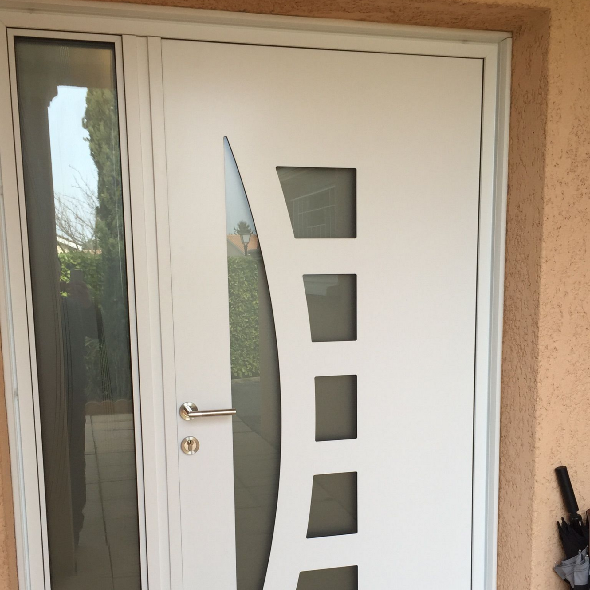 Porte d'entrée blanche avec panneau latéral, insert en verre incurvé, quatre petites fenêtres carrées, poignée argentée.