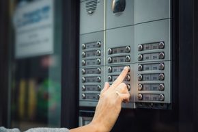 Mano presionando un botón en un intercomunicador de apartamento con múltiples botones.