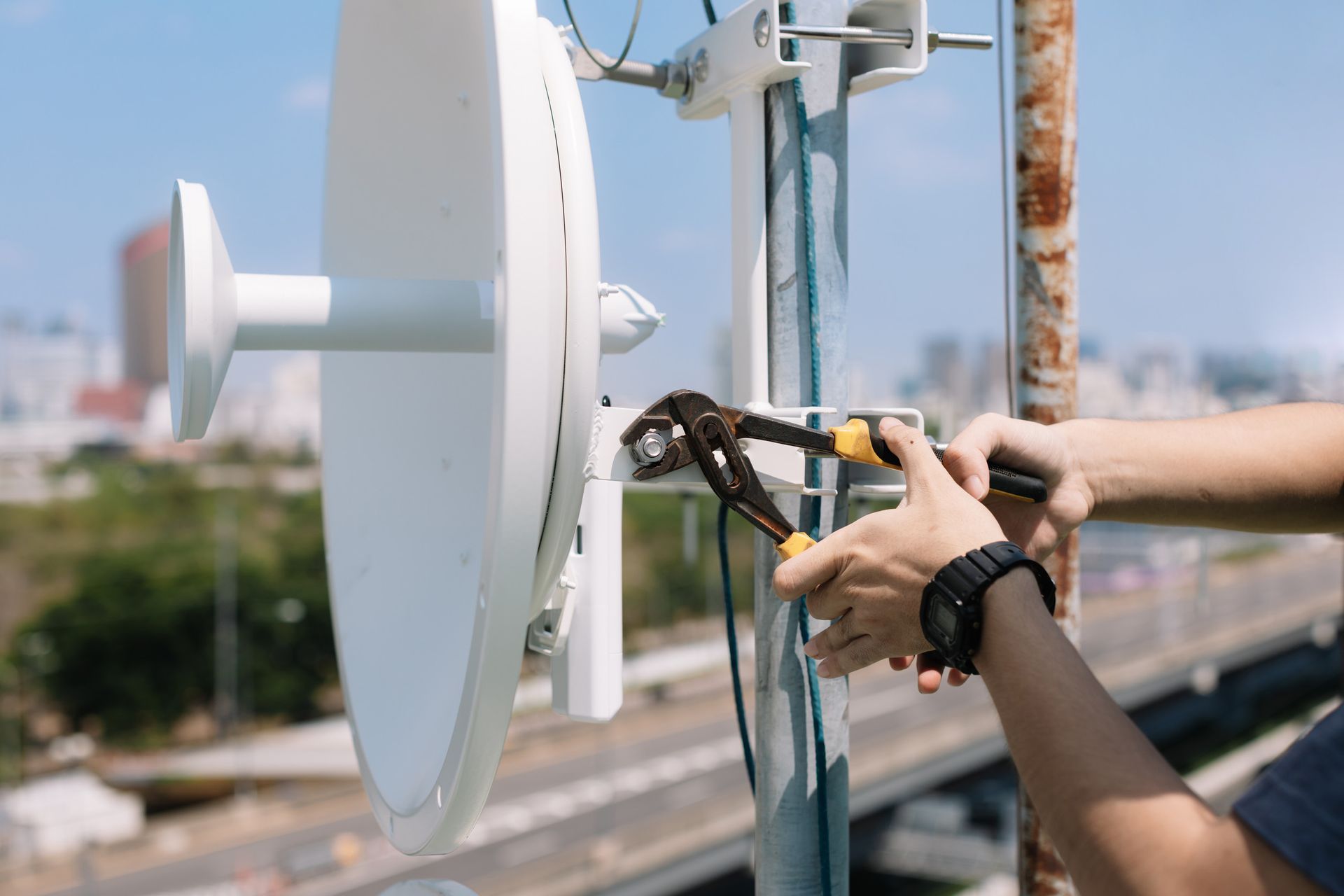 Persona que utiliza unos alicates para apretar un perno en una antena blanca, al aire libre en un día soleado.