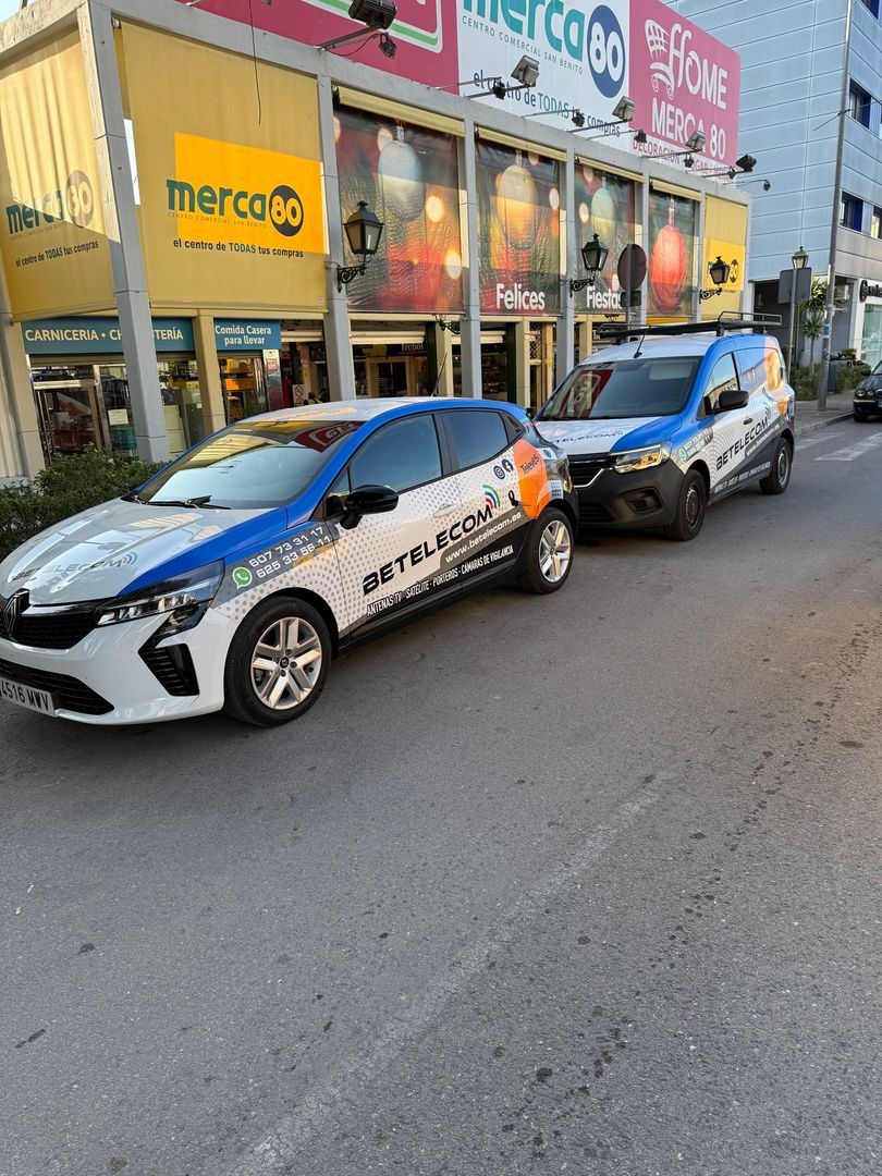 Dos camionetas de reparto azules y blancas estacionadas en una calle frente a una tienda con un cartel de 