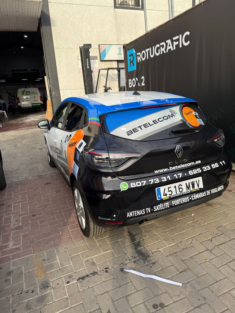 Coche Renault negro con gráficos promocionales aparcado delante de un edificio.
