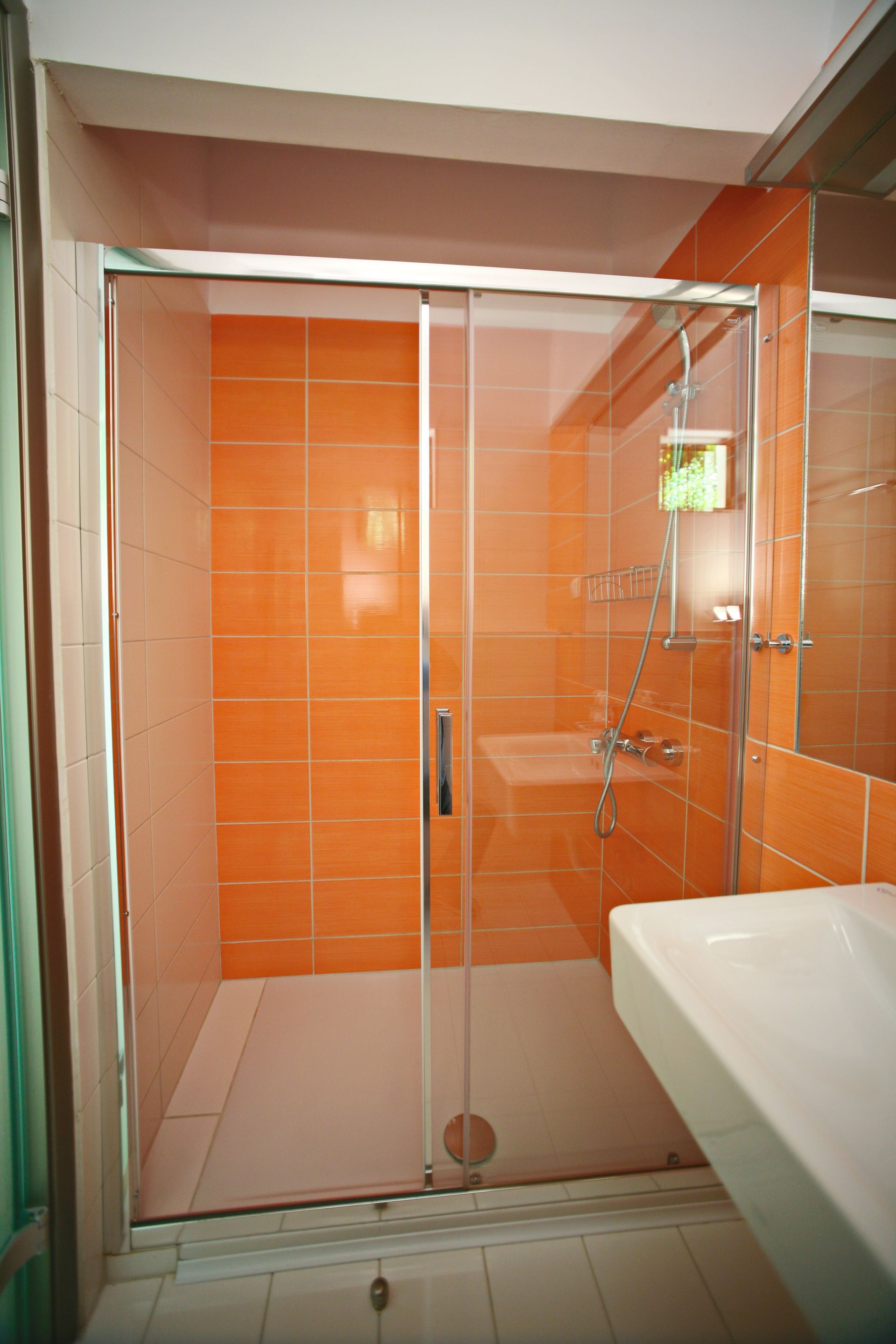 Ντους με πορτοκαλί πλακάκια και γυάλινη πόρτα στο μπάνιο.