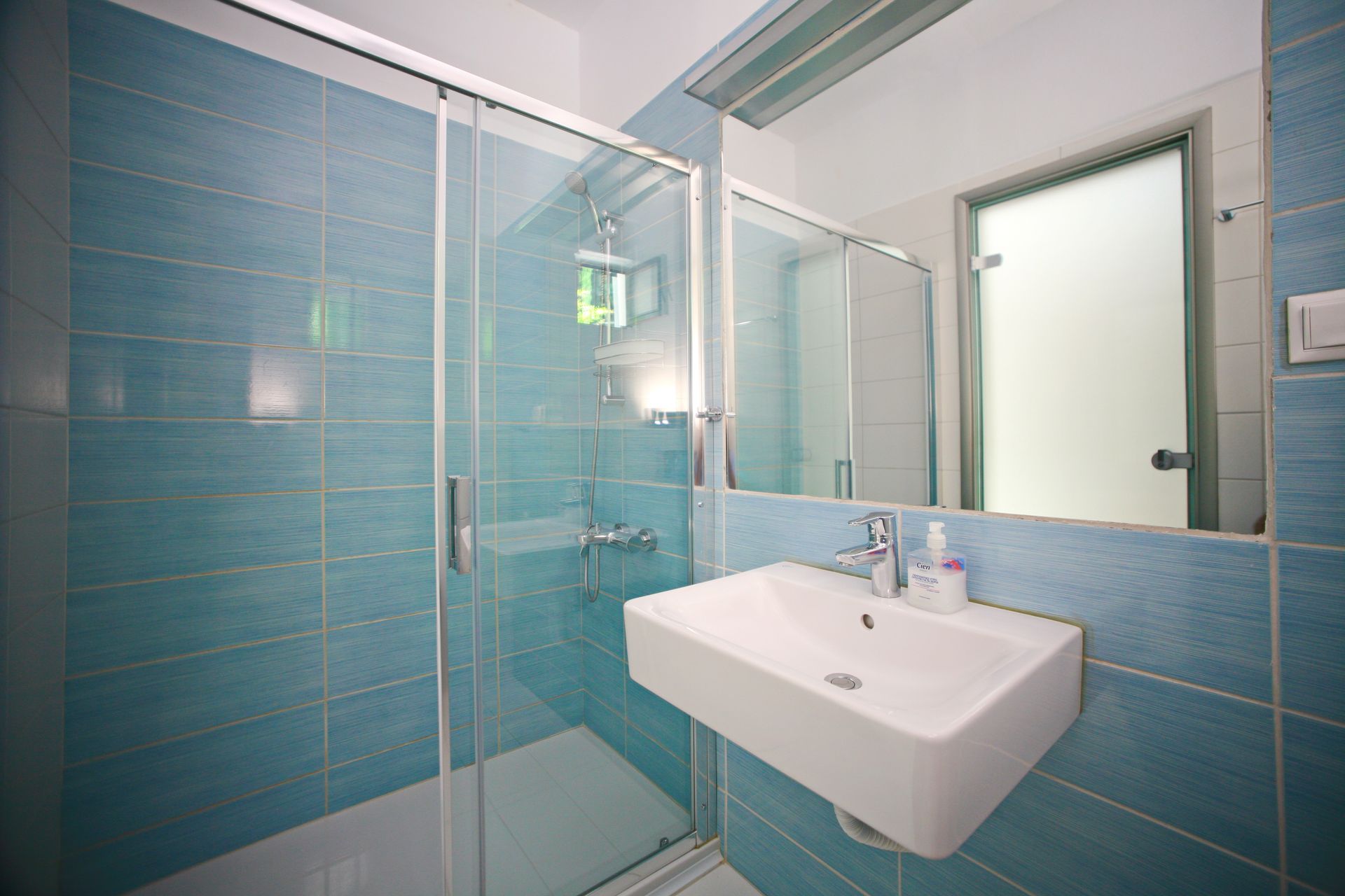 Μπλε πλακάκια μπάνιου με γυάλινη ντουζιέρα, πλωτό νιπτήρα και μεγάλο καθρέφτη.