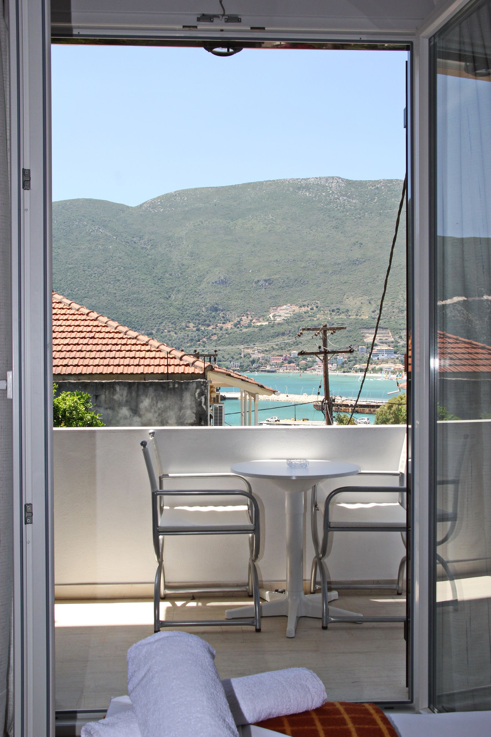 Μπαλκόνι με θέα στα βουνά, τη θάλασσα και την πόλη. Δύο καρέκλες και ένα τραπέζι βρίσκονται στο μπαλκόνι.