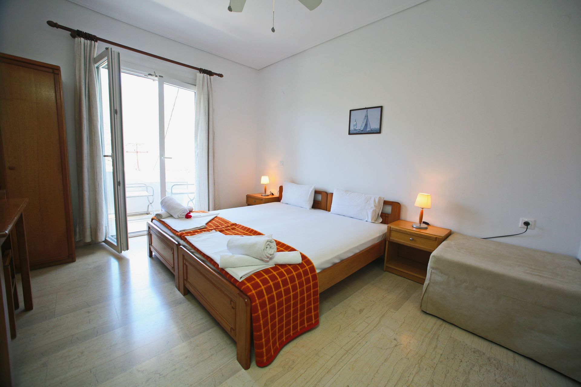 Υπνοδωμάτιο με διπλό κρεβάτι, κομοδίνα και πρόσβαση στο μπαλκόνι. Λευκοί τοίχοι, έπιπλα από ανοιχτόχρωμο ξύλο και μαρμάρινα δάπεδα.