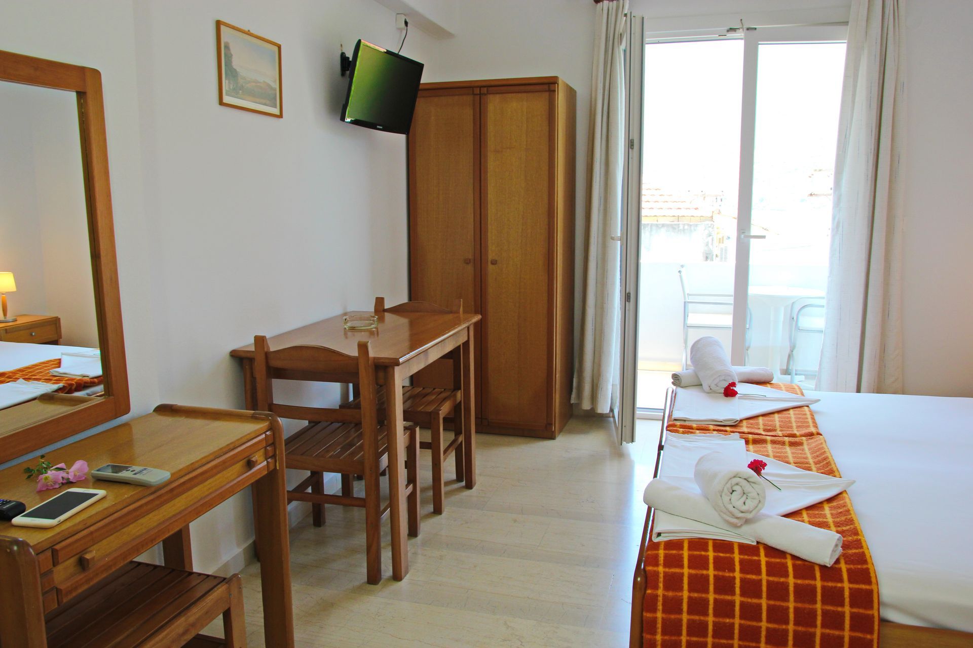 Ένα δωμάτιο ξενοδοχείου με δύο μονά κρεβάτια, τραπέζι, ντουλάπα και πρόσβαση σε μπαλκόνι.