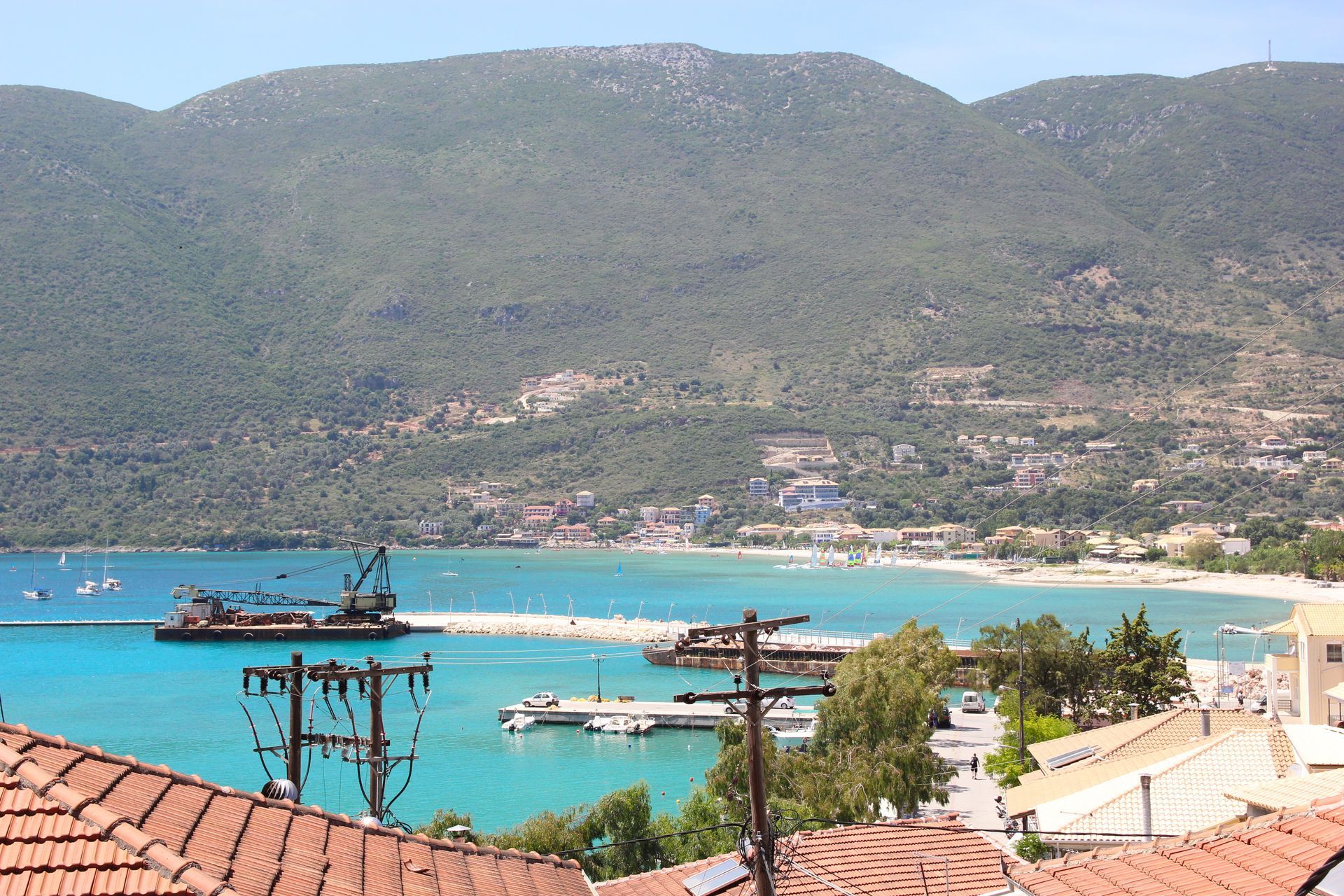 Θέα σε έναν κόλπο με τιρκουάζ νερά, ορεινό φόντο και μια πόλη στην ακτή.