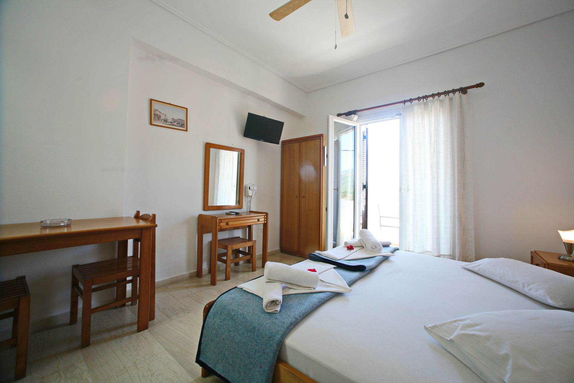 Υπνοδωμάτιο με κρεβάτι, γραφείο, νιπτήρα, ντουλάπα και ανοιχτή πόρτα σε εξωτερικό χώρο με κουρτίνες.