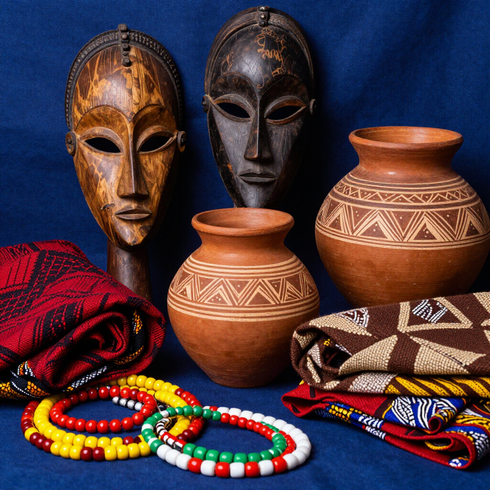 Máscaras talladas al estilo africano, vasijas de barro, coloridas pulseras de cuentas y tela tejida con estampados sobre un fondo azul.