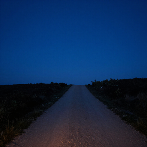 Un camino de grava que asciende hacia un horizonte oscuro bajo un cielo crepuscular de un azul intenso.