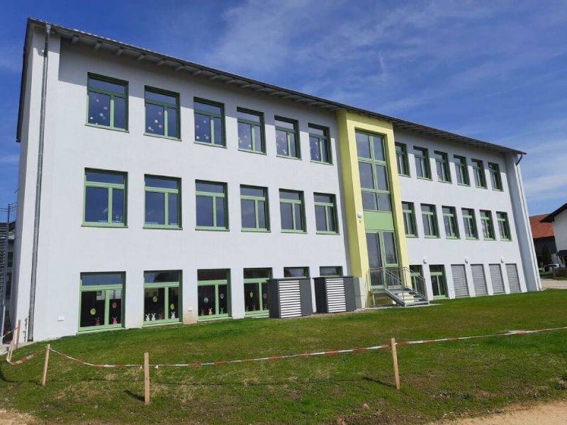 Modernes weißes Bürogebäude mit blau umrandeten Fenstern und einem grünen Rasen unter blauem Himmel